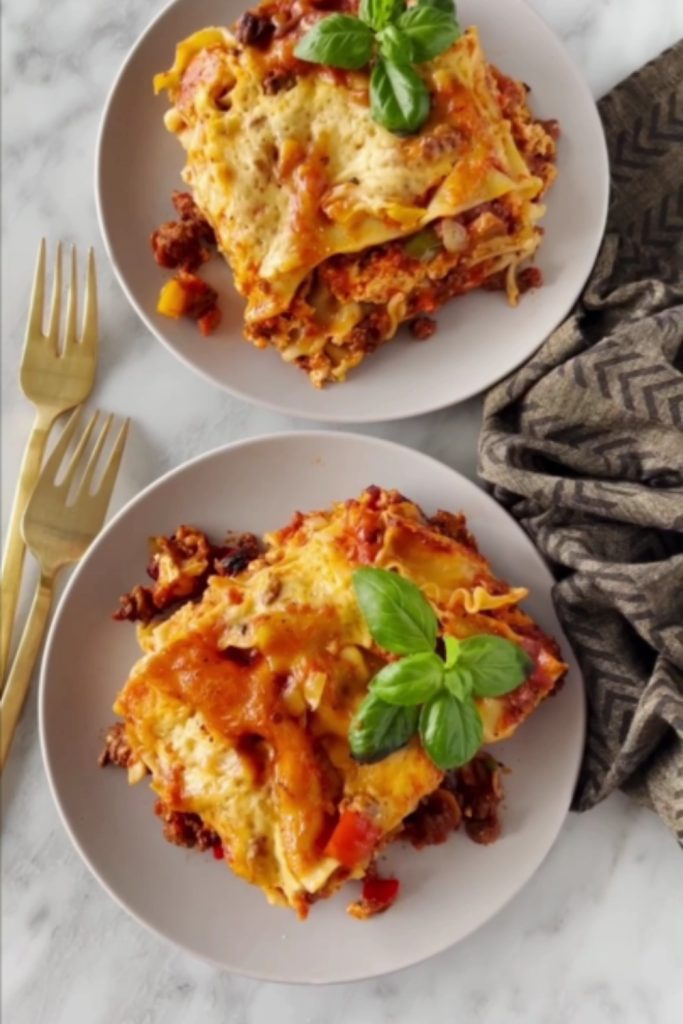 Two plates of lasagna with basil garnish and a golden fork.