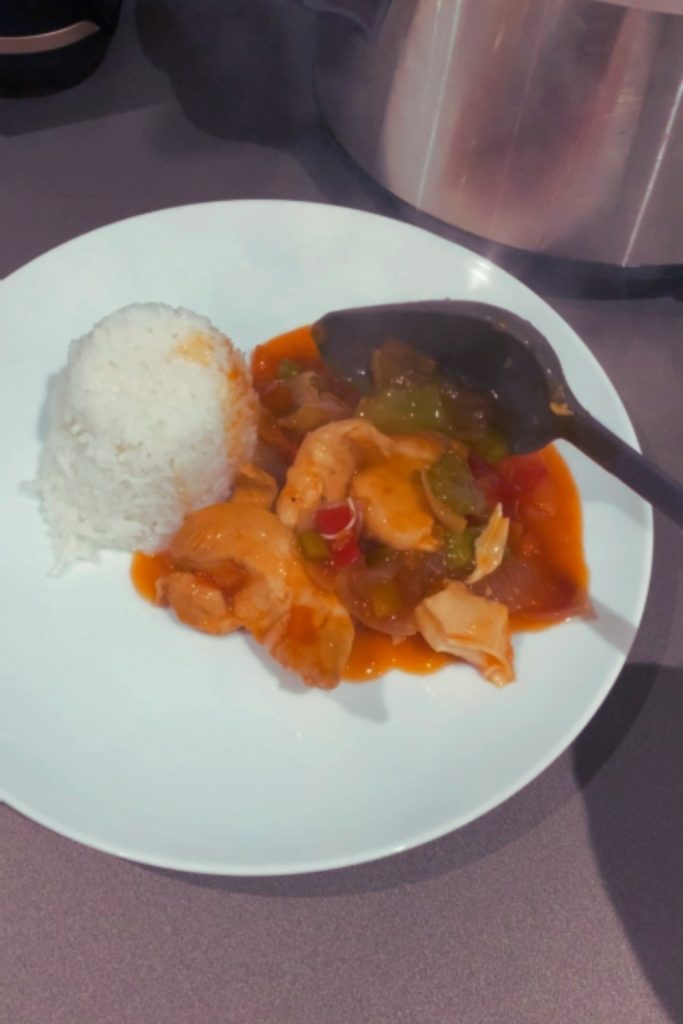 Sweet and sour chicken served with rice on a white plate.