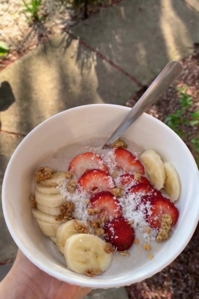 Old Fashioned Slow Cooker Barley Pudding with bananas, strawberries, coconut, and granola, held outdoors.