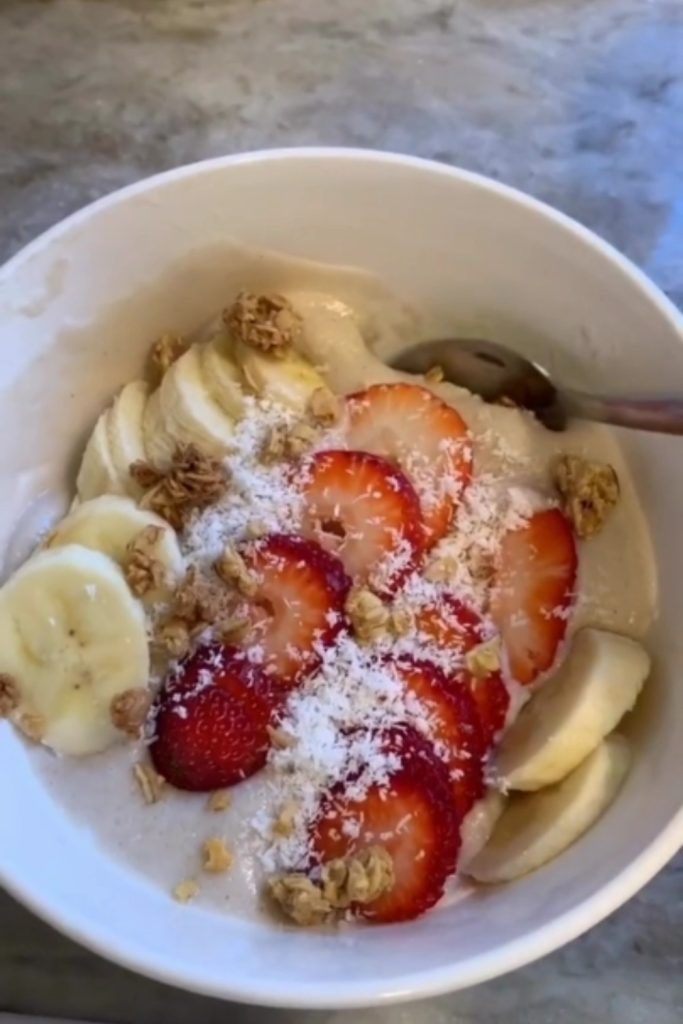 Old Fashioned Slow Cooker Barley Pudding with bananas, strawberries, coconut, and granola in a white bowl.