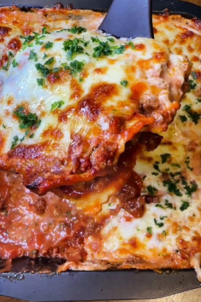 A portion of 4 Ingredients Crockpot Ravioli Lasagna being scooped with a spatula, showing melted cheese and meat sauce.