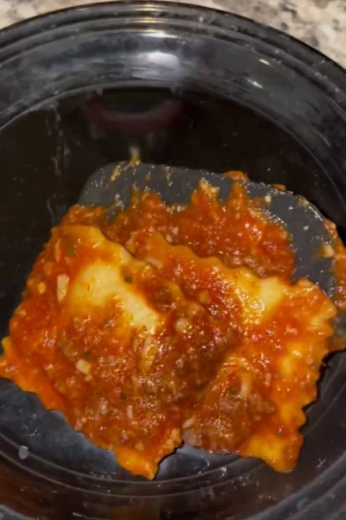 Crockpot ravioli with tomato sauce in a black bowl.