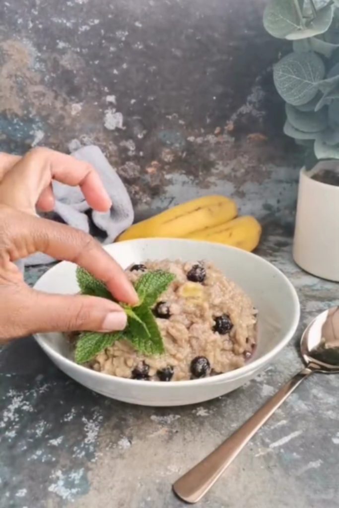 Slow Cooker Brown Rice Pudding with blueberries and a mint garnish in a white bowl.