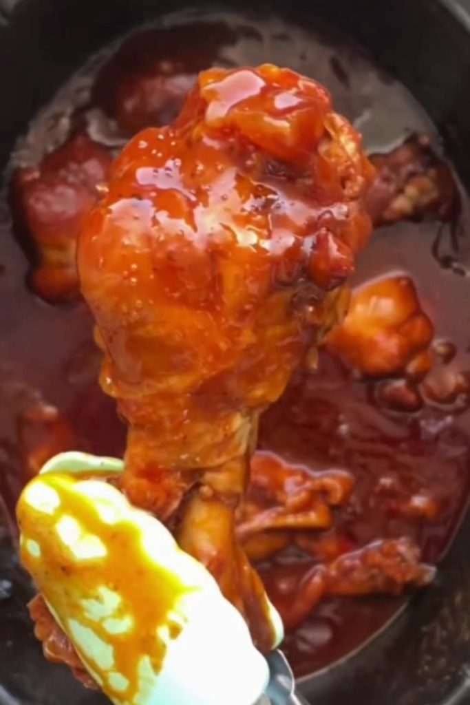 Glazed chicken leg lifted from a slow cooker with tongs.