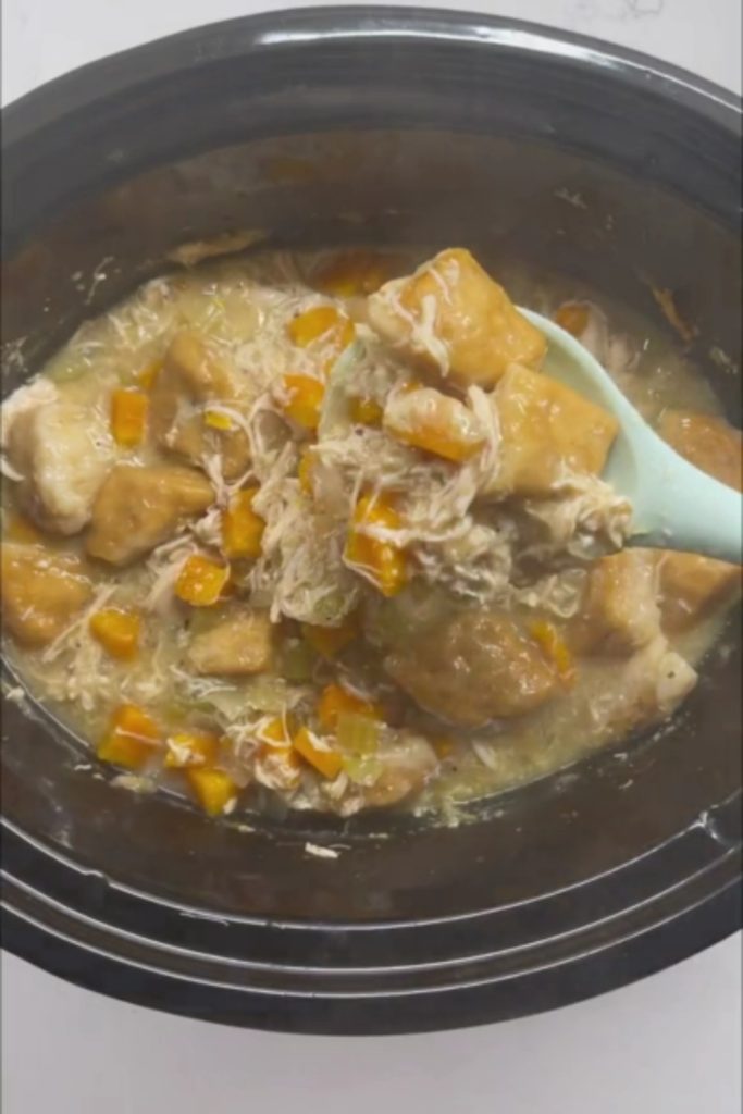 A spoon lifting a serving of 5 Ingredient Crockpot Chicken and Dumplings with shredded chicken, dumplings, and vegetables from the crockpot.